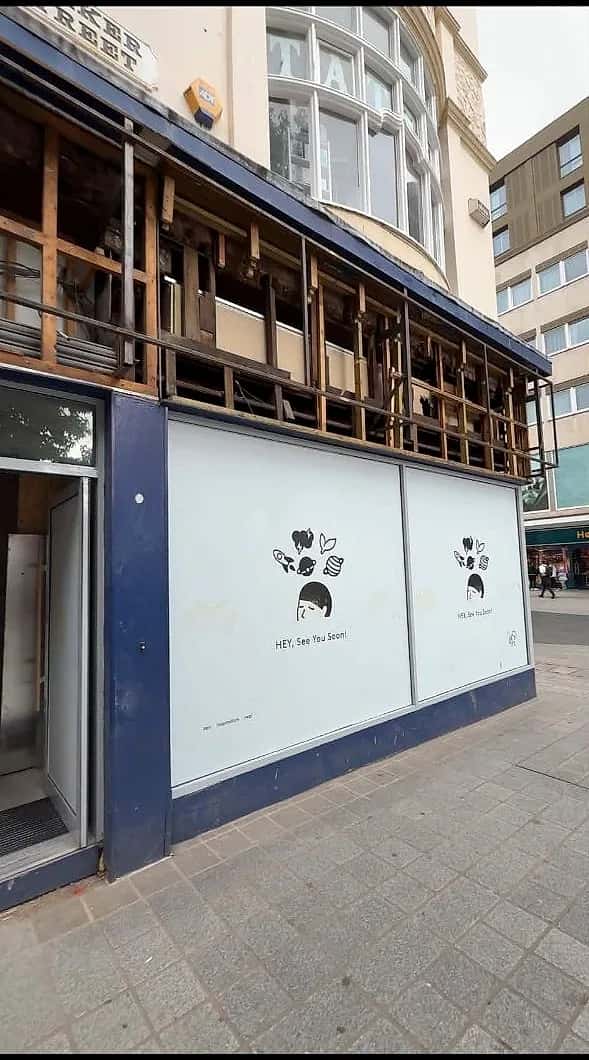 Printed hoarding across a corner unit on Parker Street, Liverpool, with the old fascia stripped back above it