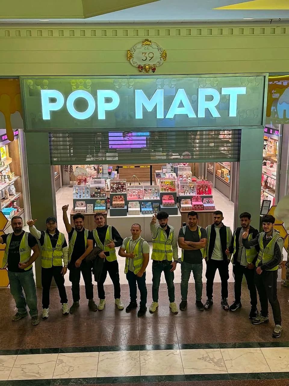 The full MO Team crew in hi-vis celebrating outside the finished, illuminated Pop Mart storefront at night