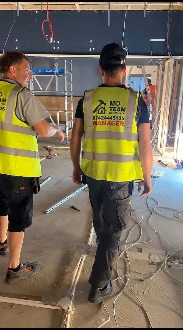 Two MO Team crew members from behind on site, the site manager's vest printed MO TEAM MANAGER