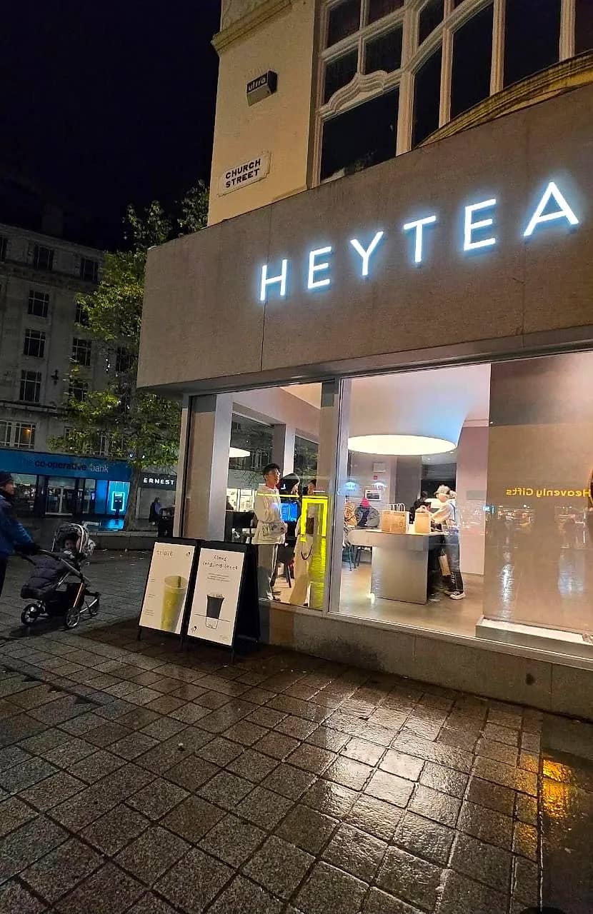 The finished HEYTEA shop trading after dark in Liverpool, sign lit and customers inside at the counter