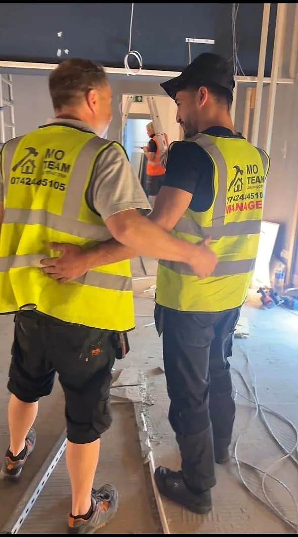 Two crew in MO Team hi-vis vests, one marked Manager, walking through a retail unit stripped back to the shell