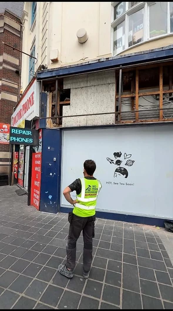 A MO Team crew member in hi-vis at the printed hoarding across the HEYTEA unit on Parker Street, Liverpool, with the strip-out under way behind it