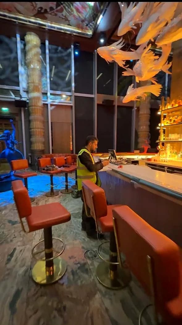 A MO Team fitter in hi-vis working at the bar top inside Sexy Fish, Mayfair, with the restaurant set for service around him