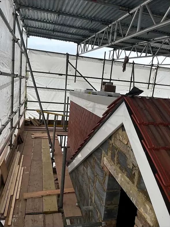 The gable end of a London terrace under scaffold and a weatherproof wrap, a new timber dormer framed against the old red roof
