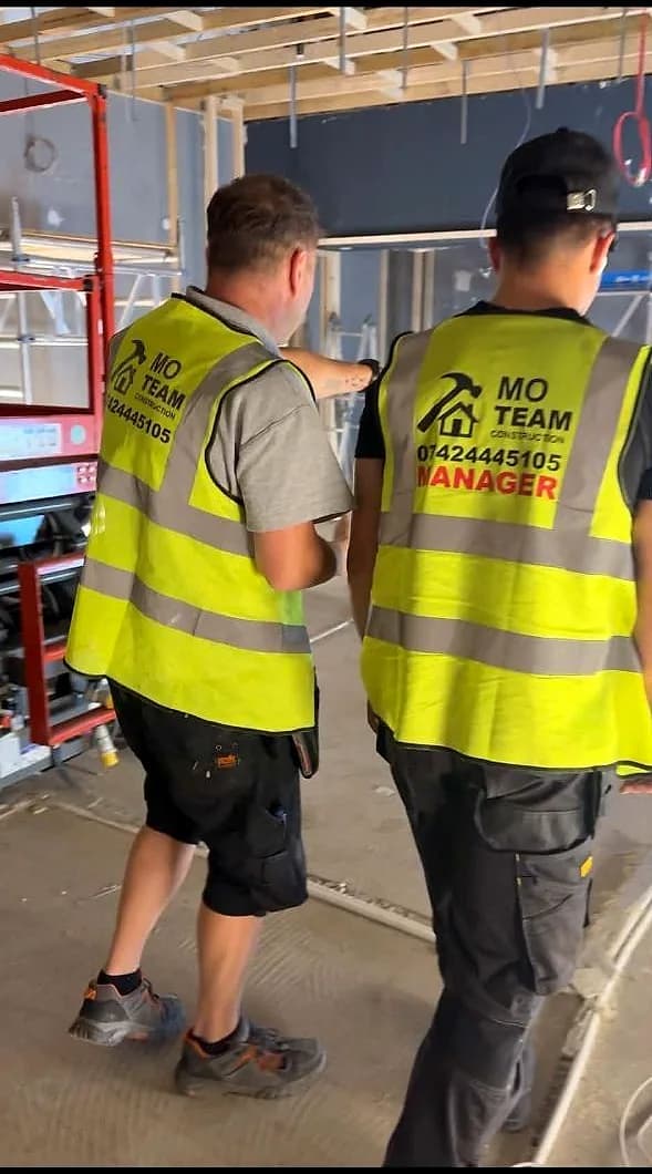 The site manager and a colleague in hi-vis pointing up at the exposed ceiling grid of a stripped unit